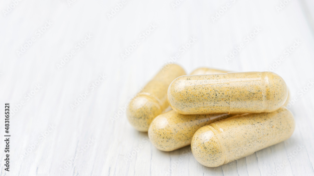 Yellow herbal capsules on white table, medication treatment, alternative medicine, close-up view Yellow herbal capsules on white table, medication treatment, alternative medicine, close-up view