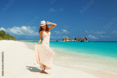 Fashion woman walking on the beach. Happy island lifestyle. White sand, blue cloudy sky and crystal sea of tropical beach. Vacation at Paradise. Ocean beach relax, travel to Maldives islands