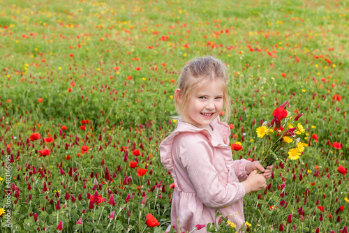 little blonde girl in a pink dress stands in a blooming field with a bouquet of flowers