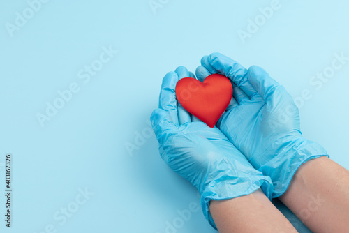 red heart in hands in blue medical gloves on a blue background. background for the day of the medic, top view, space for text