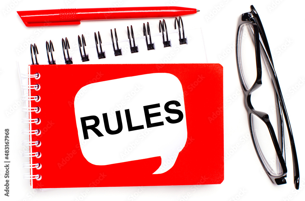 On a white background, white and red notepads, black glasses, a red pen and a white card with the text RULES On a white background, white and red notepads, black glasses, a red pen and a white card with the text RULES