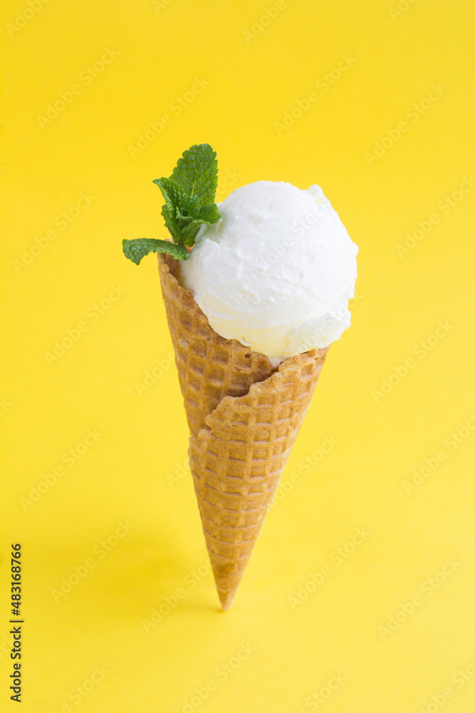 Close-up on vanilla ice cream in a waffle cone on the yellow background. Location vertical. Close-up on vanilla ice cream in a waffle cone on the yellow background. Location vertical.