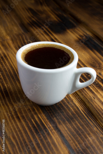 Close-up on black coffee in the white cup on the wooden background. Location vertical.
