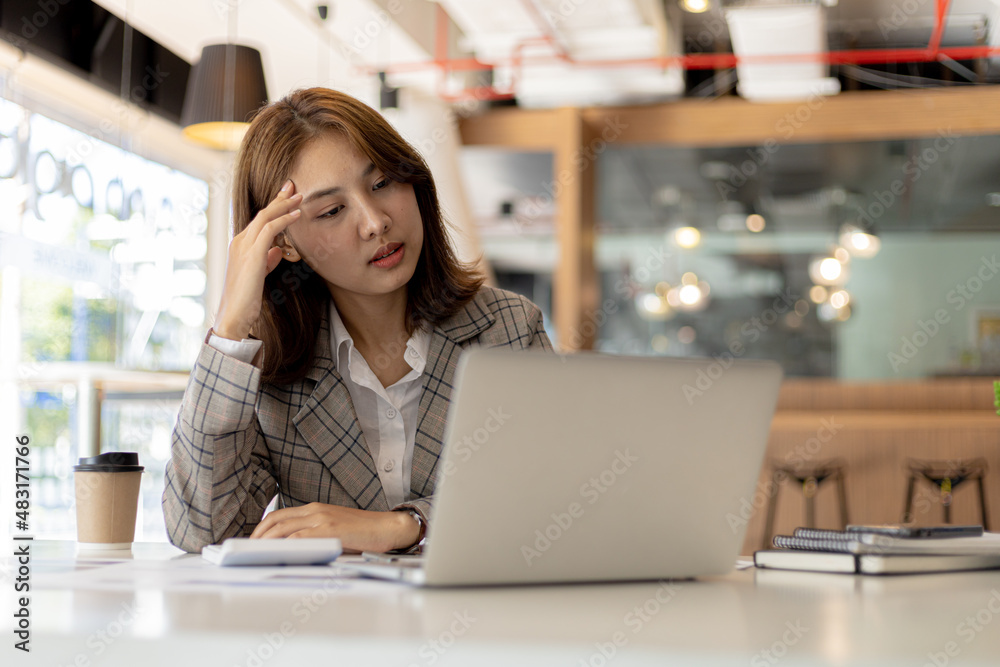 A businesswoman has a headache after working in front of her laptop for a long time and looking at a lot of paperwork causing stress, she is resting and working hard. Office syndrome concept. A businesswoman has a headache after working in front of her laptop for a long time and looking at a lot of paperwork causing stress, she is resting and working hard. Office syndrome concept.