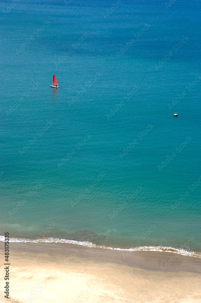Background with a small red sail in the middle of a huge transparent blue sea
