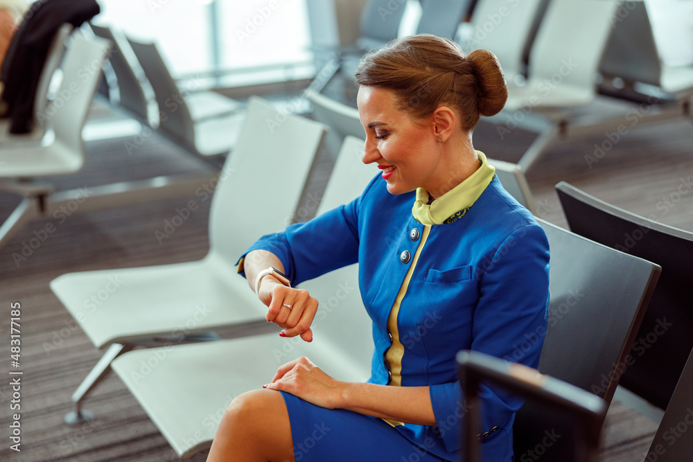 Female flight attendant in air hostess uniform looking at watch and smiling  while waiting for airplane in airport departure lounge Photos | Adobe Stock
