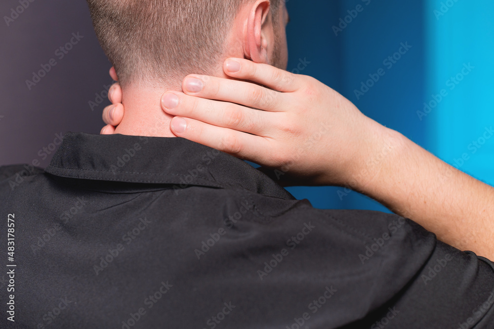 Fototapeta premium Close-up. A freelance man in a dark shirt has a sore neck after working for a long time, he massages his neck himself.