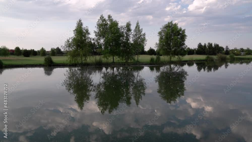 View of the lake and golf field. Panning the pond, trees in the shoreline and fairway. Beautiful reflection of the trees and sky in the water surface. View of the lake and golf field. Panning the pond, trees in the shoreline and fairway. Beautiful reflection of the trees and sky in the water surface.