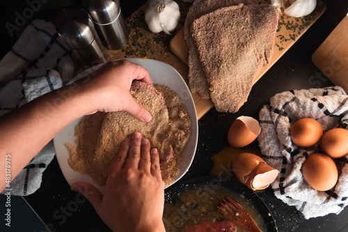 hands breading an schnitzel, ingredients in the background