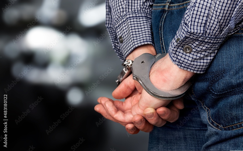 Arrested man in handcuffs with handcuffed hands behind back in prison background