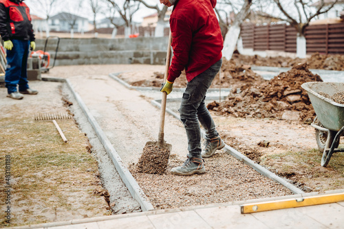 Worker using pavement slabs and shovel to build stone sidewalk. Close up of construction worker installing and laying pavement stones on terrace, road or sidewalk.