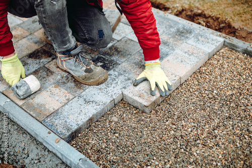 Industrial worker installing concrete paver blocks with rubber hammer