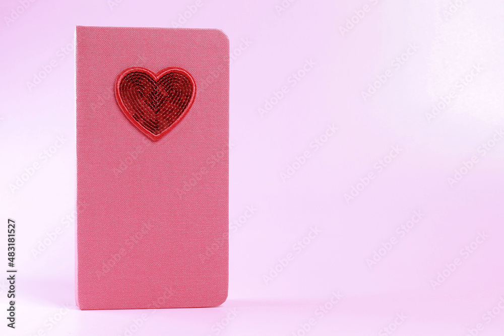 Red notebook with a heart, on a pink background, the concept of Valentine's day, March 8, a holiday card with a place for text