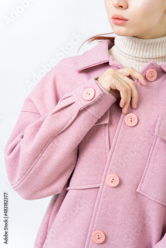 The sleeve of thick women warm pink coat with large buttons. A woman in turtleneck is buttoning her coat. White background.
