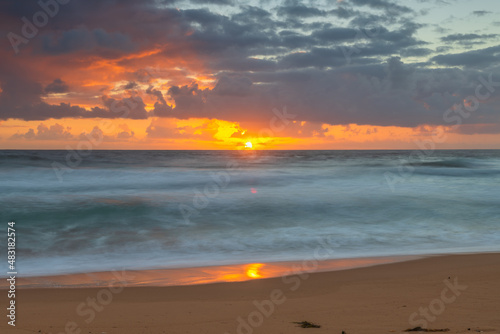 Sunrise at the seaside with waves and clouds © Merrillie