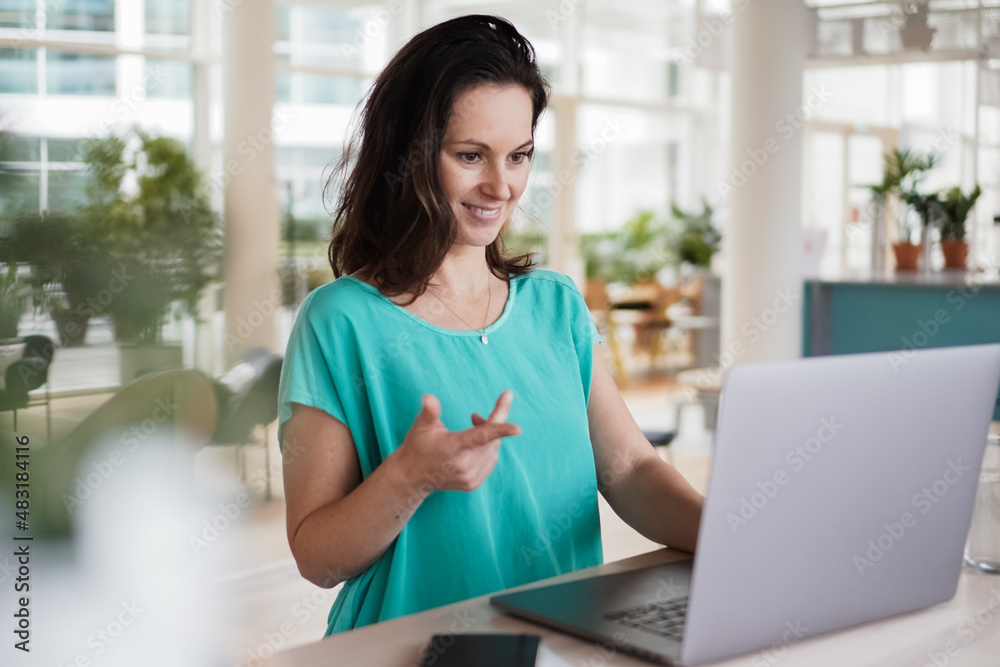 happy smiling remote working woman talking to laptop or notebook in casual outfit sitting on her work desk in her modern loft living room home office having a video chat happy smiling remote working woman talking to laptop or notebook in casual outfit sitting on her work desk in her modern loft living room home office having a video chat