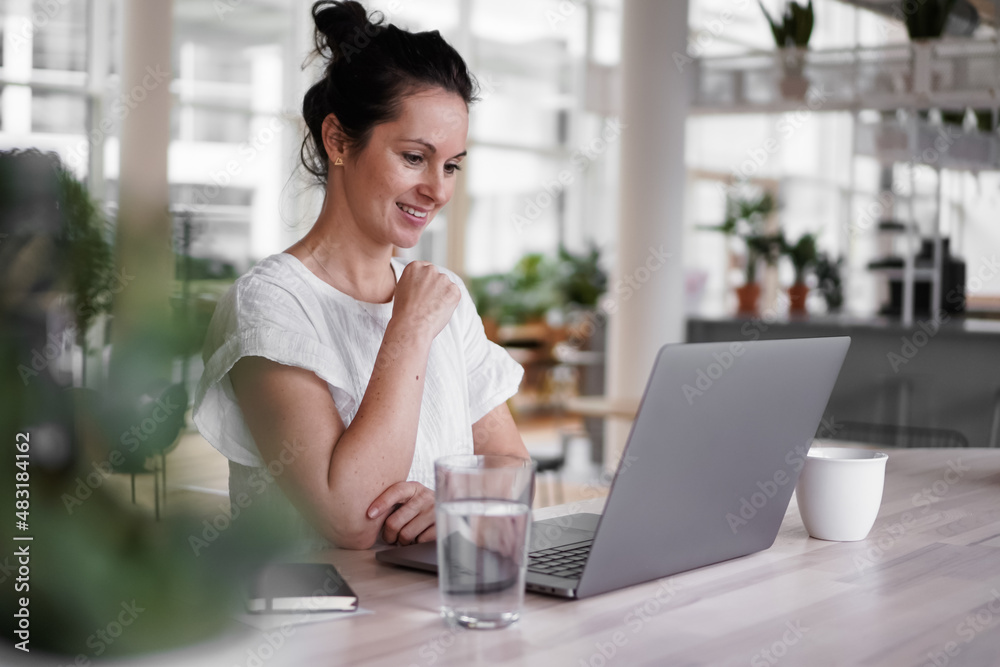 happy smiling remote working woman talking to laptop or notebook in casual outfit sitting on her work desk in her modern loft living room home office having a video chat happy smiling remote working woman talking to laptop or notebook in casual outfit sitting on her work desk in her modern loft living room home office having a video chat