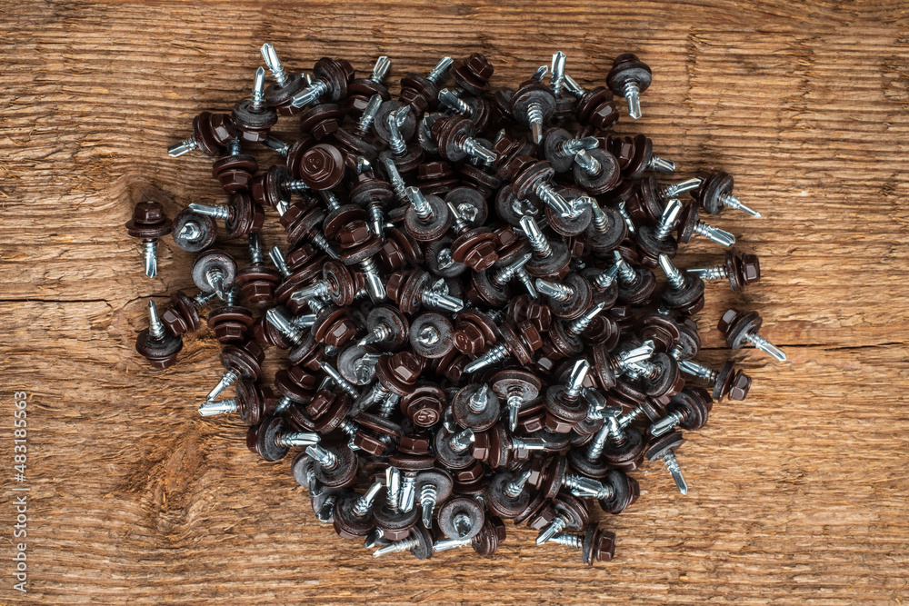 А bunch of self-tapping screws for fixing the roof with brown hex heads. Against the background of a rough wood texture..