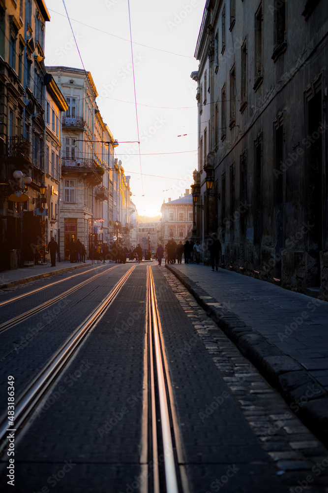 dramatic street of old city in sunset evening time with atmospheric lighting, vertical photography perspective view foreground tram rails transport landmark infrastructure