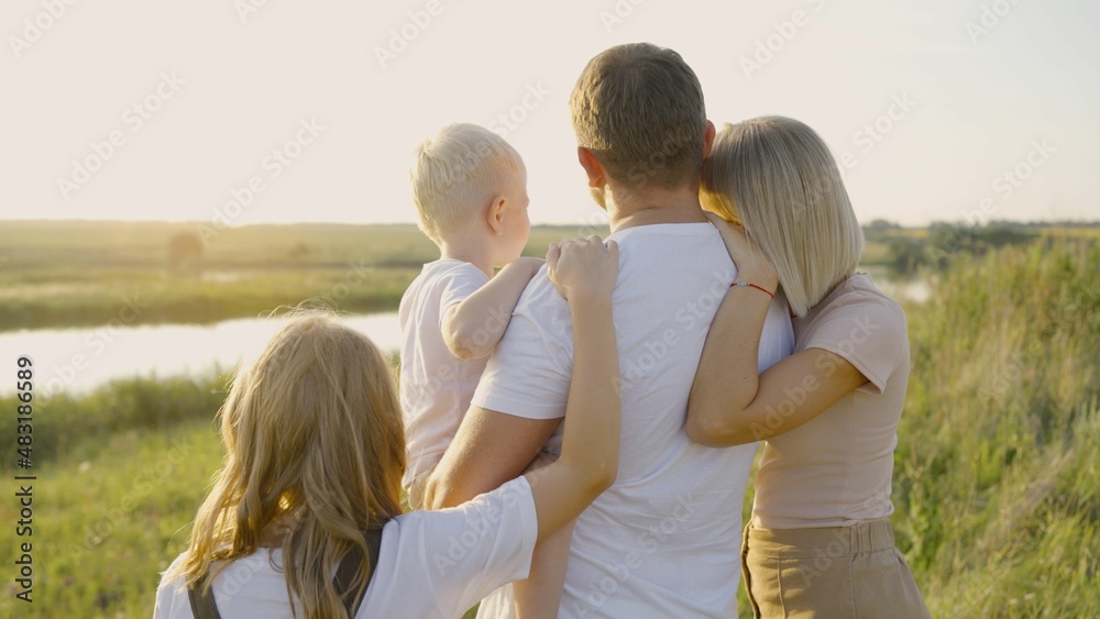 Parents hug their children in the countryside. Happy family concept. A happy family is looking at the field. Parents hug their children in the countryside. Happy family concept. A happy family is looking at the field.