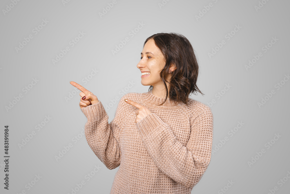 Wide smiling woman is pointing with both hands on the grey background behind her. Wide smiling woman is pointing with both hands on the grey background behind her.