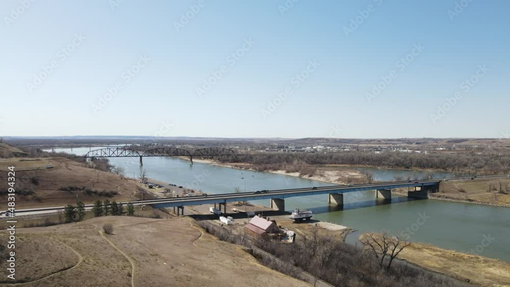 View of two bridges over river in autumn with a bright blue sky. Rolling hills along the river with meandering paths. Ship yard and parking lot next to the water. View of two bridges over river in autumn with a bright blue sky. Rolling hills along the river with meandering paths. Ship yard and parking lot next to the water.