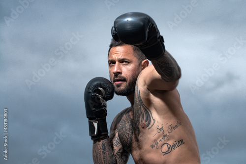 Muscular kick boxer or muay thai fighter punching. Kickboxing fighter in boxing gloves hitting shadow, training for competition. Boxing training outside.