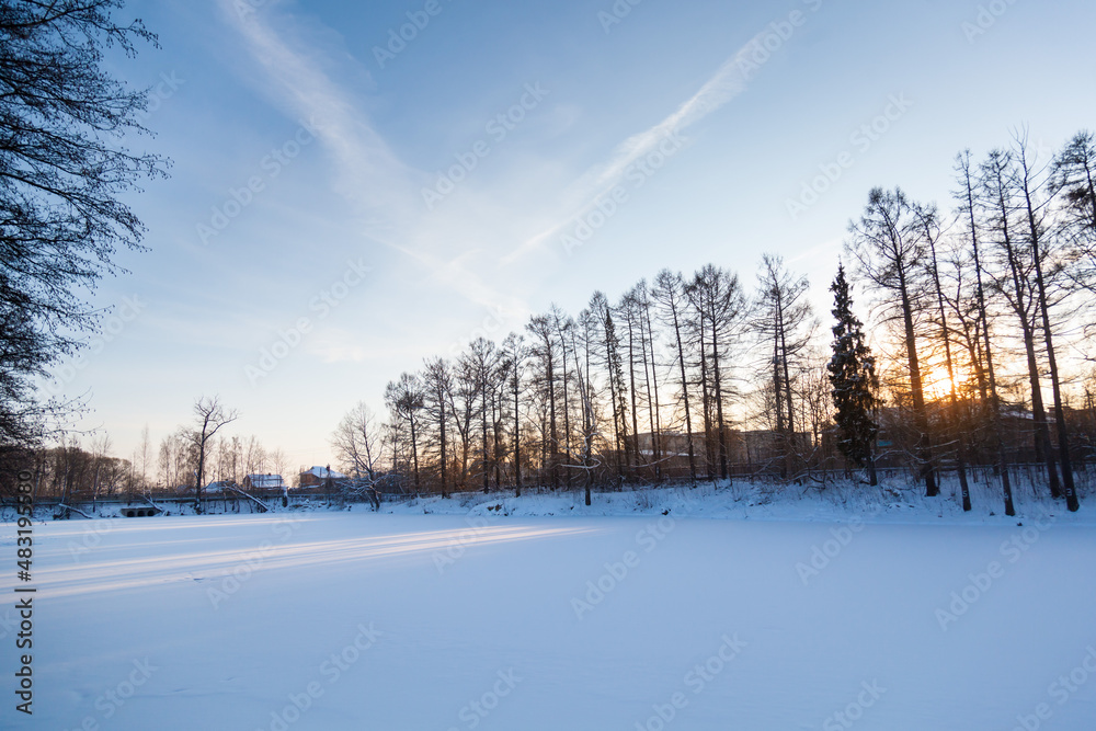 Fototapeta premium Frozen pond under a large layer of snow on the background of sunset.