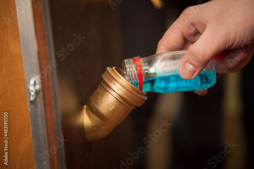 A man pours blue water from a bottle into a pipe.