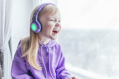 A girl in a sweatshirt of very peri color listens to music in headphones