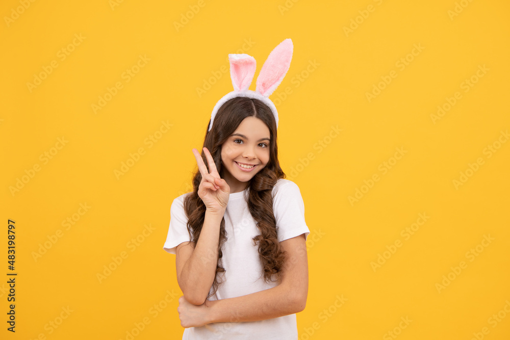 cheerful child in bunny ears on yellow background show peace, easter