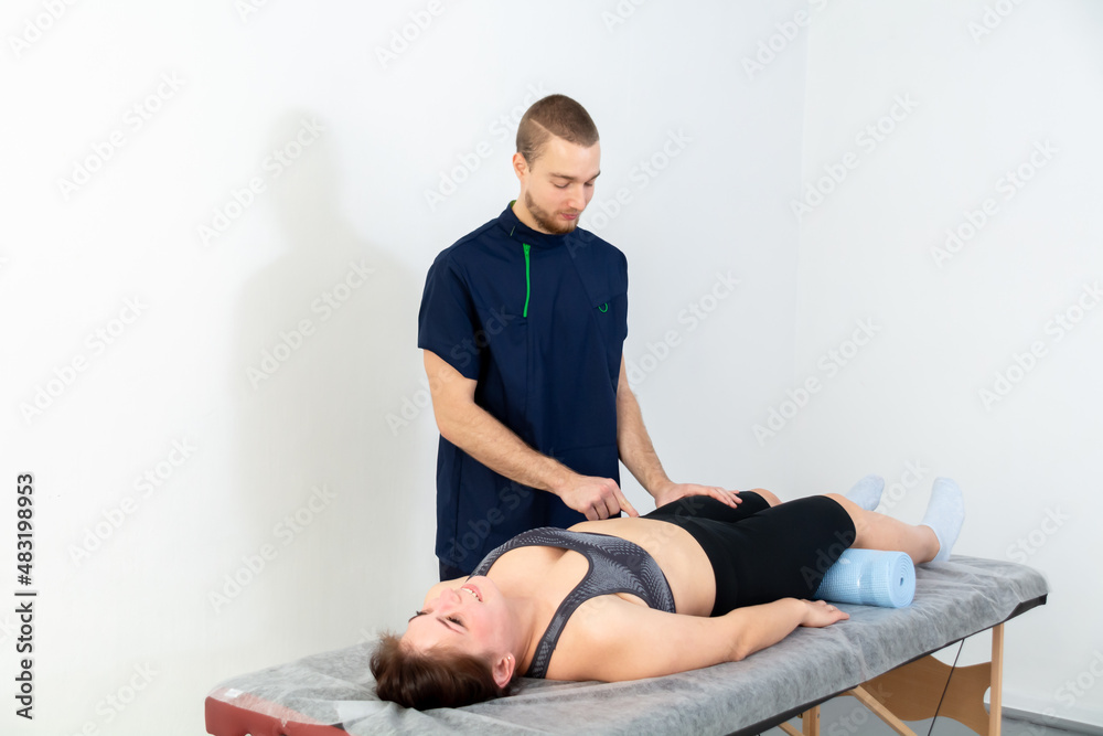 A male massage therapist in a blue suit makes a sports massage to a woman. Back pain treatment.