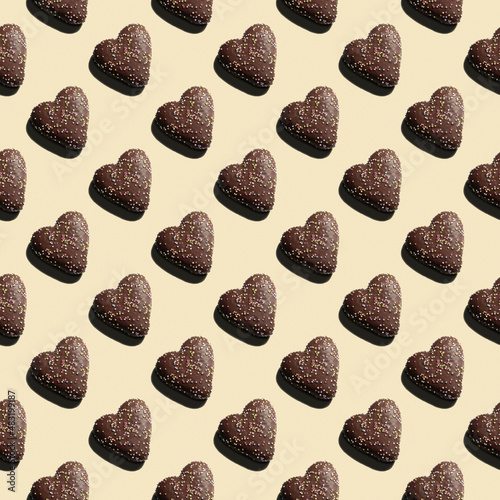Seamless pattern with heart shaped gingerbread in chocolate glaze and colored sprinkles. Flat Lay oblique position.