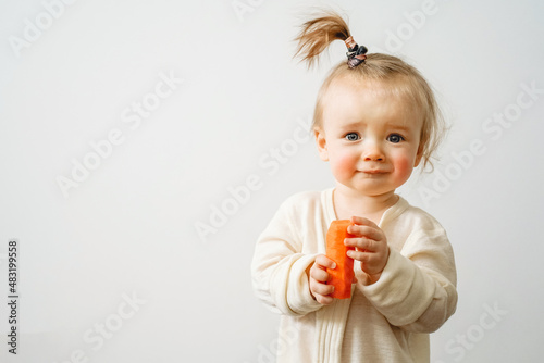 a baby with a food allergy holds a carrot in her hands, the child has red cheeks, irritation