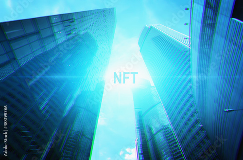 NFT word on modern futuristic background of high skyscrapers in blue color. Non fungible token concept.