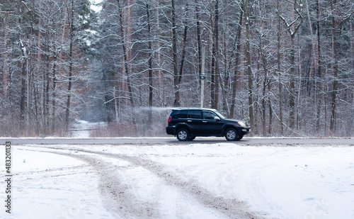 Blurred motion of a black SUV on a highway in winter on background of snowy forest