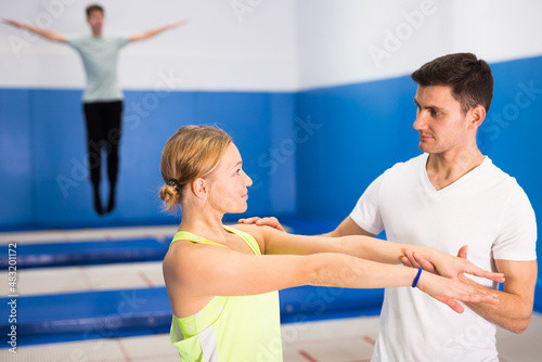 Male instructor helping woman warming up before trampoline training in fitness center