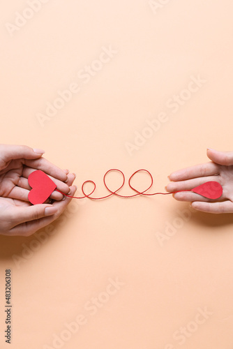Female hands with red paper heart and drop of blood on color background. Donation concept