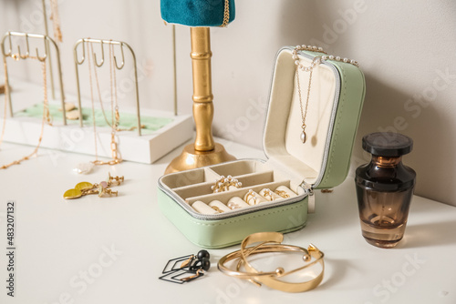 Box with different stylish jewelry on white table near light wall