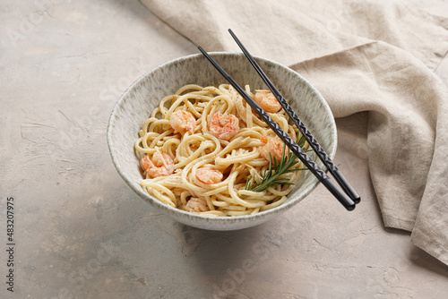 Deep grey japanese style bowl with pasta spaghetti with heavy cream and roasted shrimps with garlic sauce and parmesan cheese, black chopsticks on grey concrete surface