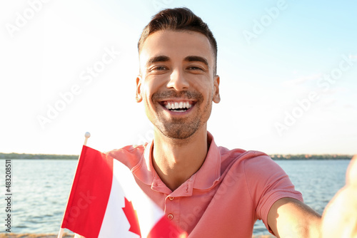 Young man with flag of Canada taking selfie near river