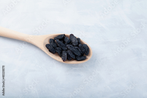 Sweet black raisins in wooden spoon on gray textured background. Dried grapes fruit. Selective focus, copy space