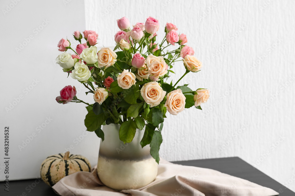 Vase with bouquet of beautiful roses and pumpkin on table