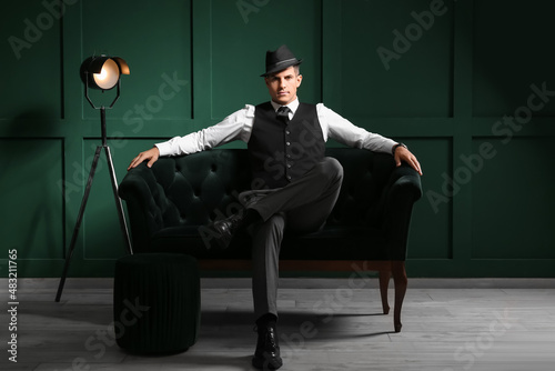 Obraz na płótnie Gentleman in formal clothes and stylish hat sitting on sofa in dark room