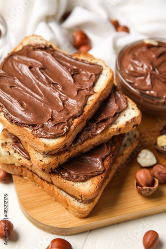 Board of bread with chocolate paste and hazelnuts on table, closeup