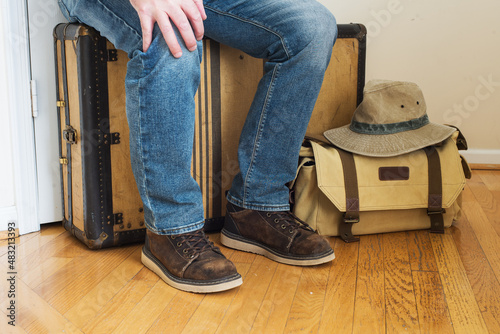 a male traveler in jeans and old boots sits on a vintage suitcase waiting for departure