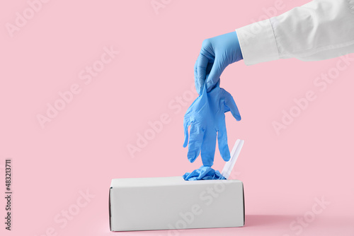 Doctor taking medical glove from box on pink background