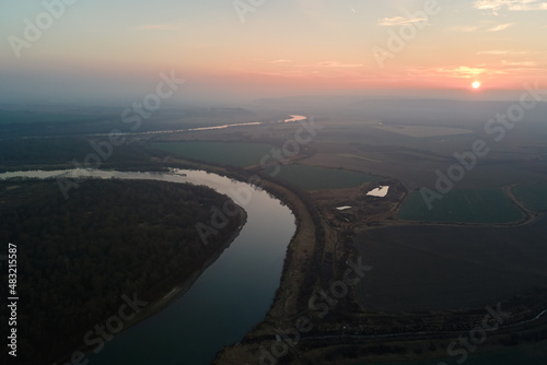 Aerial view of wide river flowing quietly in rural countryside in autumn evening