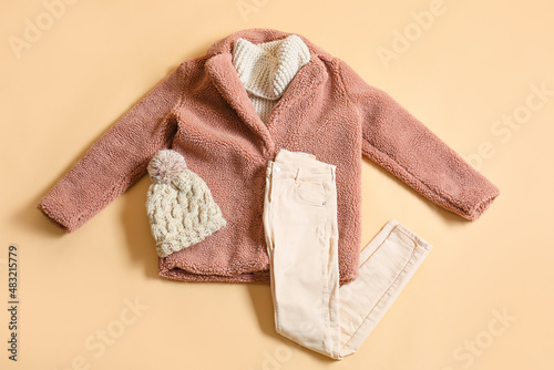 Winter coat, sweater, pants and knitted hat on beige background