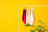 Clothes rack with knitted sweaters and houseplant on color background
